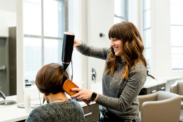 Parrucchiera sorridente che asciuga i capelli di una cliente