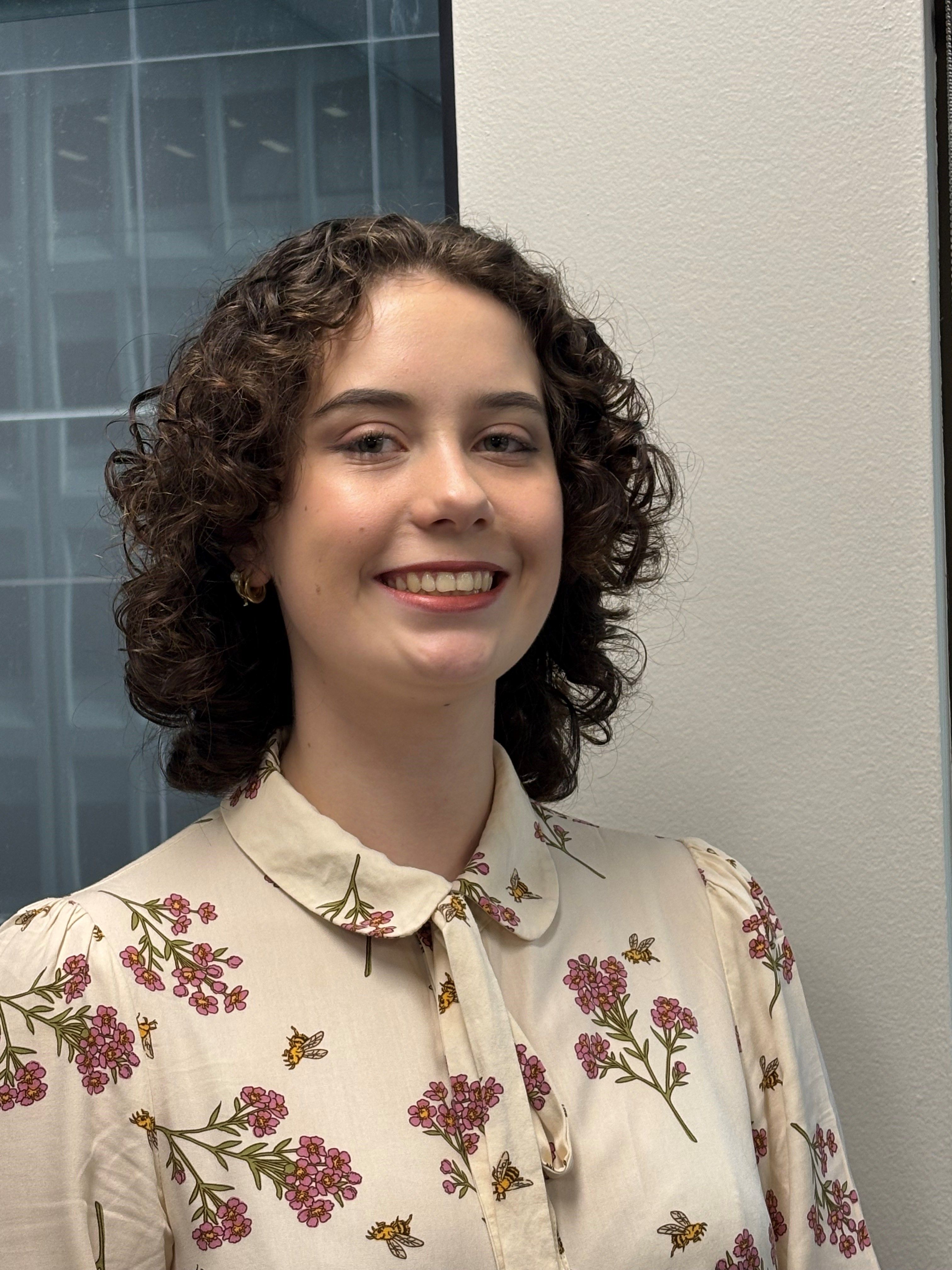 A woman smiling standing in front of an office window.