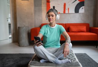 Person seated on floor at home using headphones and smart phone to meditate