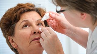 Medical professional helping apply older person's eye drops