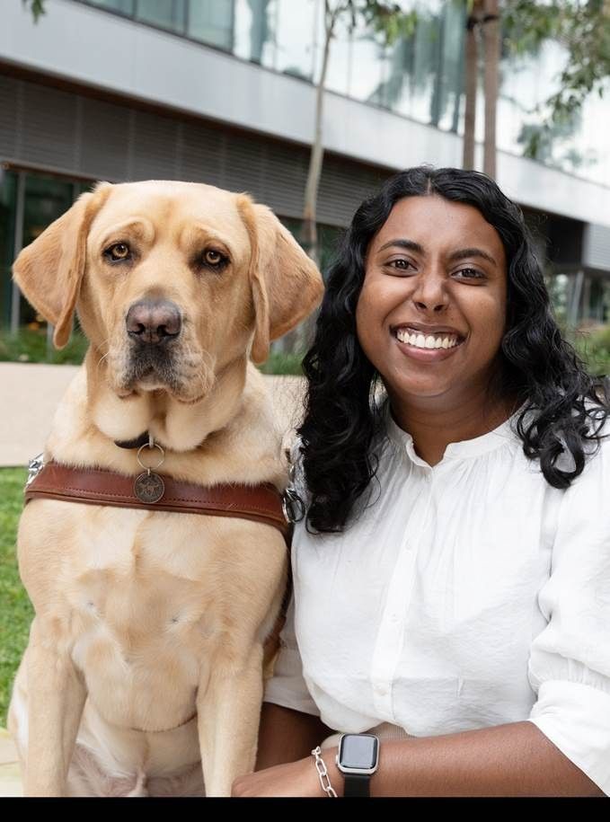 Abby Jayasuriya smiling at the camera with her yellow Labrador Guide Dog Duke.