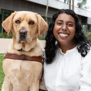 Abby Jayasuriya smiling at the camera with her yellow Labrador Guide Dog Duke.