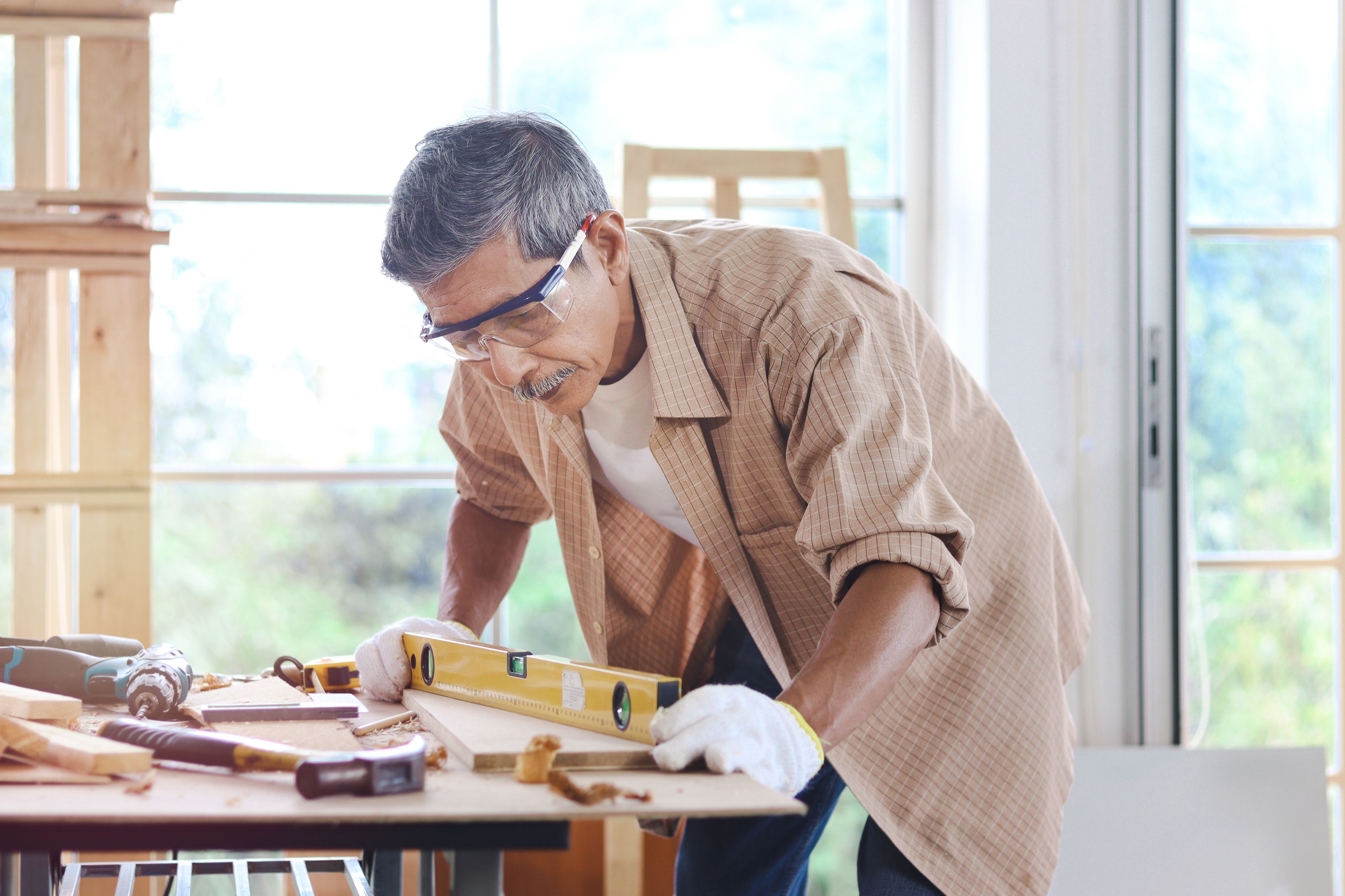 A older man with safety glasses working in a carpentry shop, measuring a table