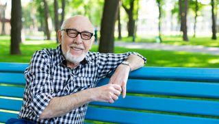 Older man in checkered shirt with glasses sitting on a park bench.