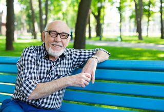Older man in checkered shirt with glasses sitting on a park bench.