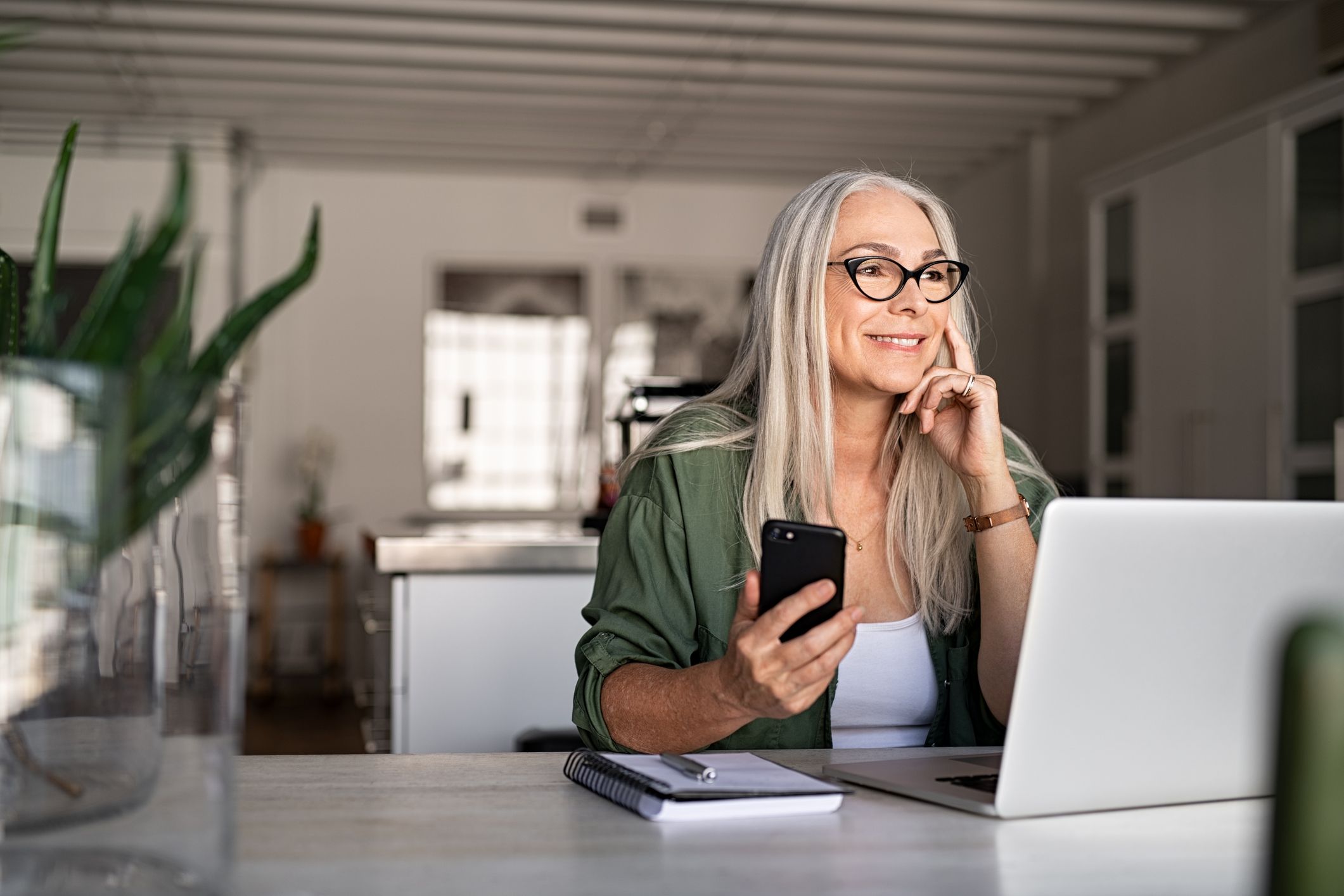 A woman working from home using a laptop and smartphone.