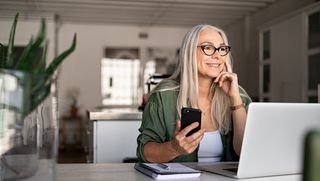 A woman working from home using a laptop and smartphone.