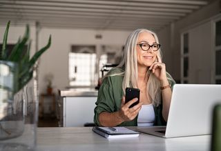 A woman working from home using a laptop and smartphone.