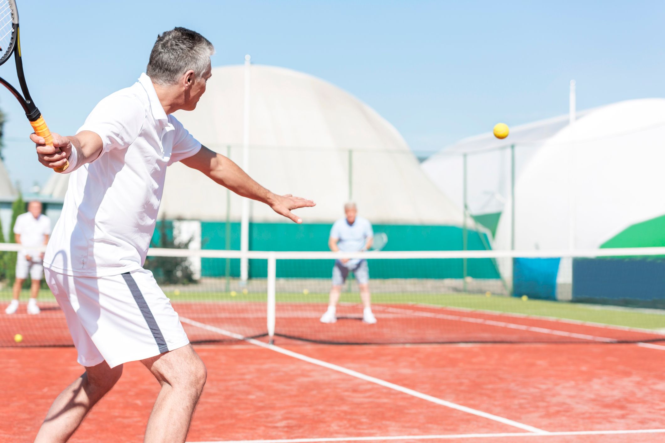 A man playing tennis outside on a clay court.