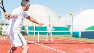 A man playing tennis outside on a clay court.