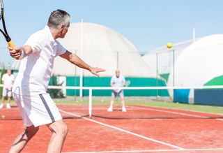 A man playing tennis outside on a clay court.