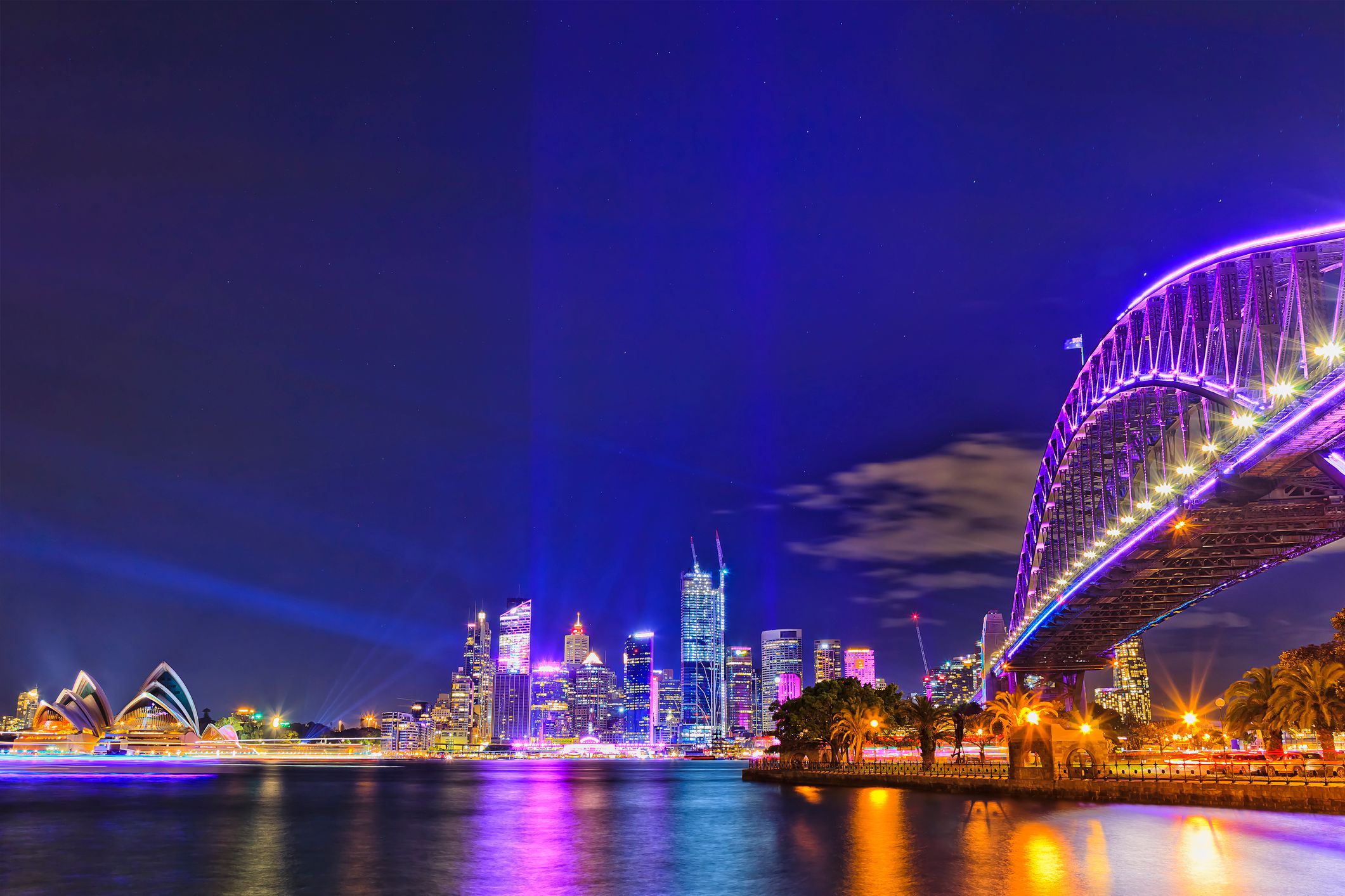 An image of the Sydney Harbour lit up with a purple and blue colour scheme for Vivid, including the Sydney Harbour Bridge and Sydney Opera House.