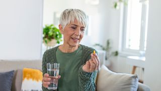 Woman looking at supplement in hand while holding glass of water