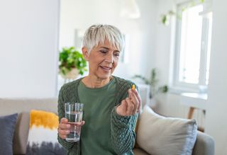 Woman looking at supplement in hand while holding glass of water