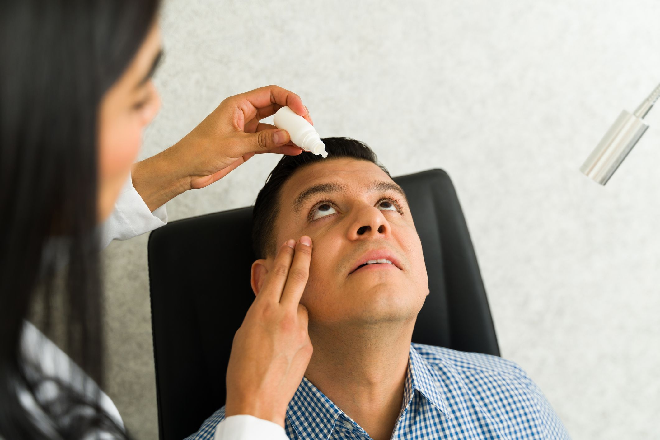 An optometrist applies dilating eye drops to a patient's eyes.