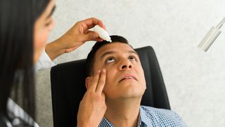 An optometrist applies dilating eye drops to a patient's eyes.