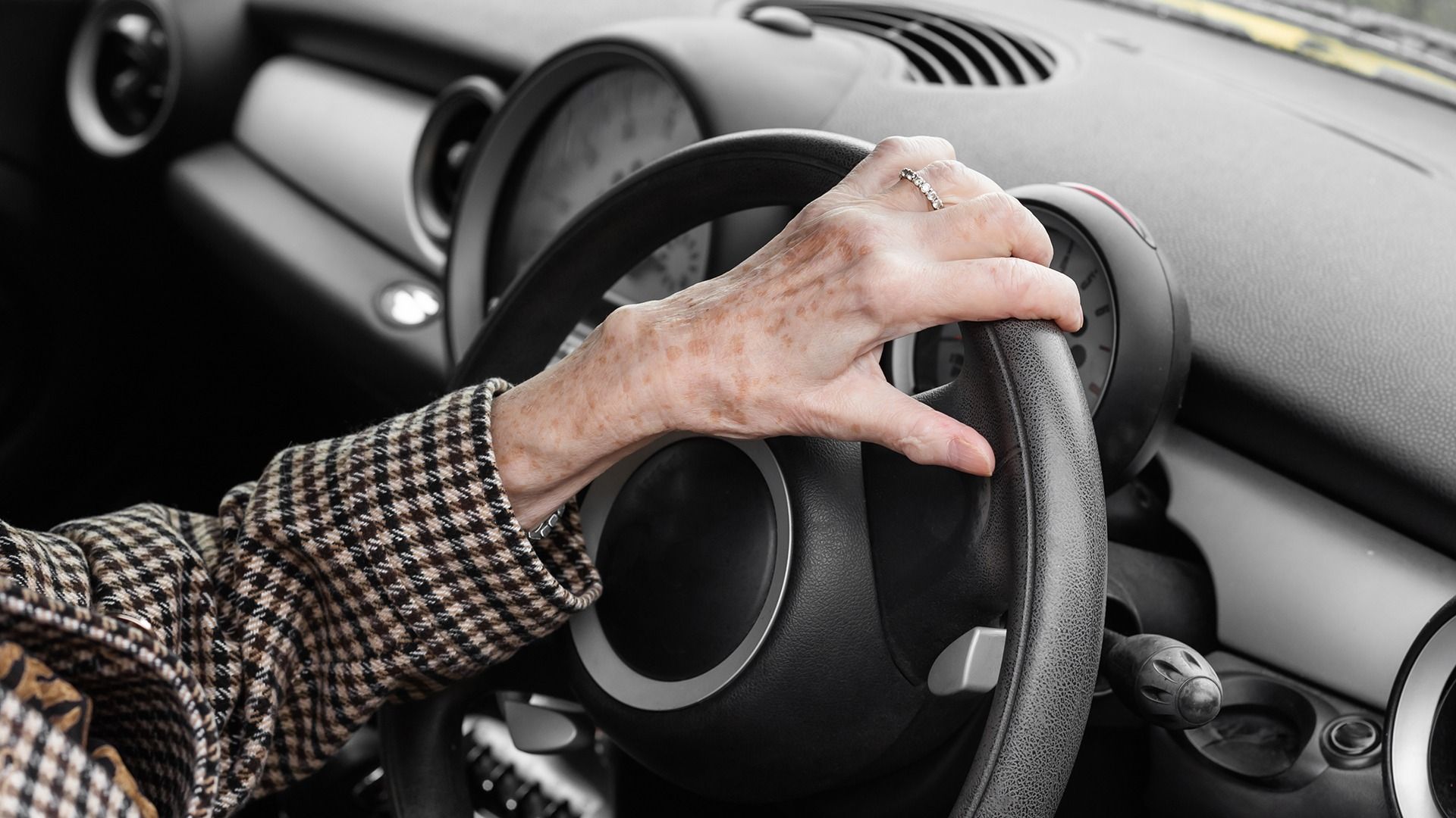 An older person's hand resting on a steering wheel.