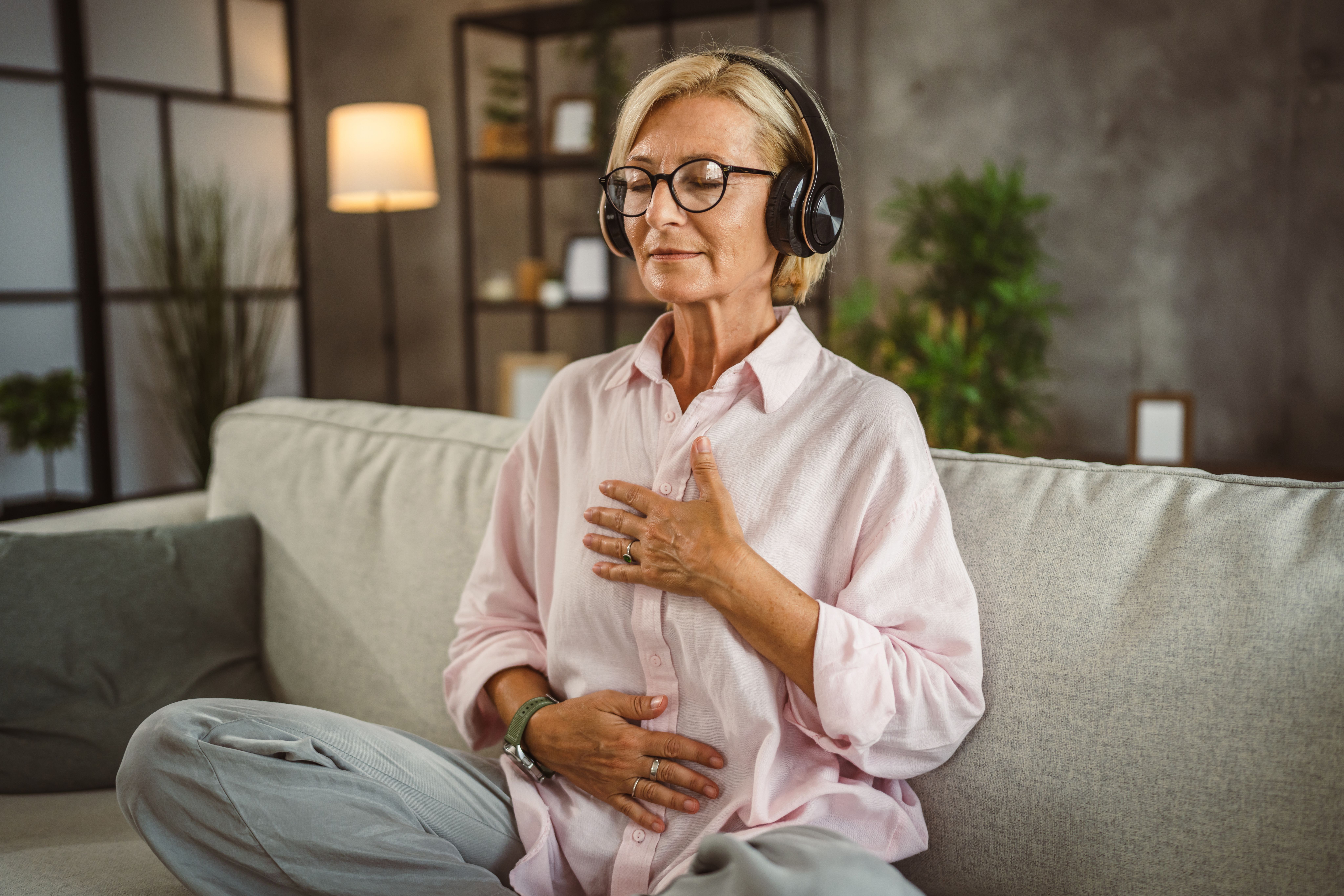 A woman sitting cross-legged on the couch with headphones in following a guided meditation