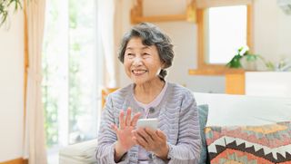 Older woman seated on a couch using a smartphone held out in front of her.