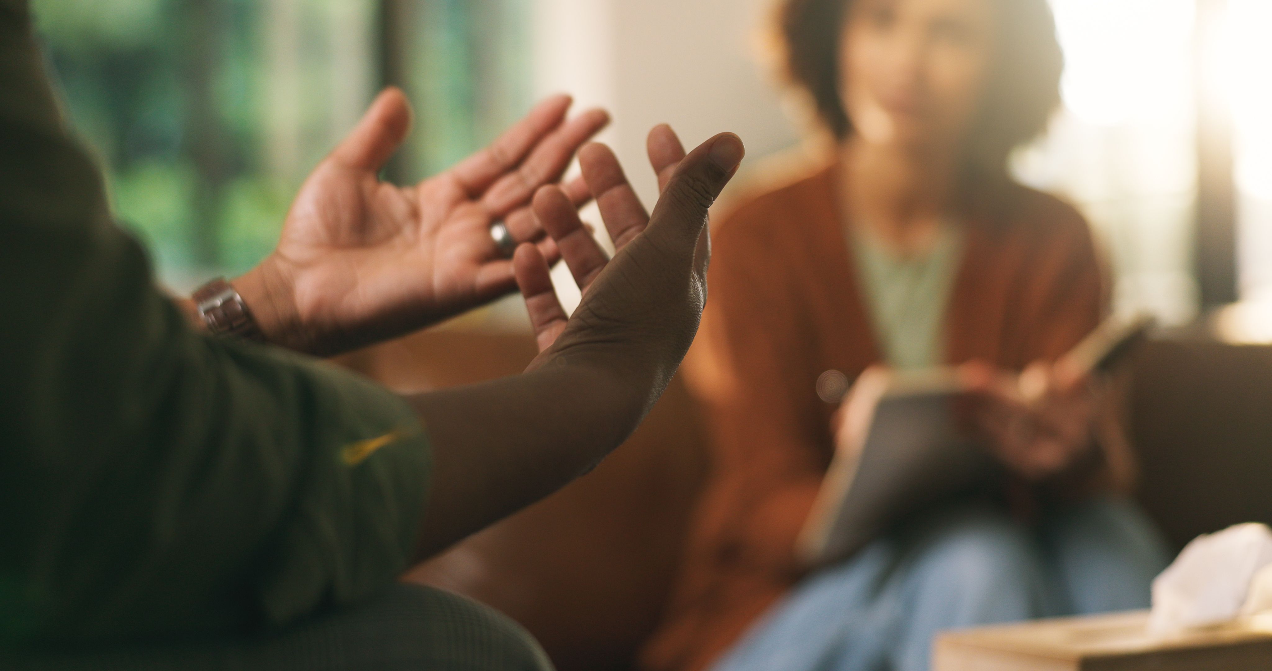 A man's hand gestures talking to a counsellor on a couch.