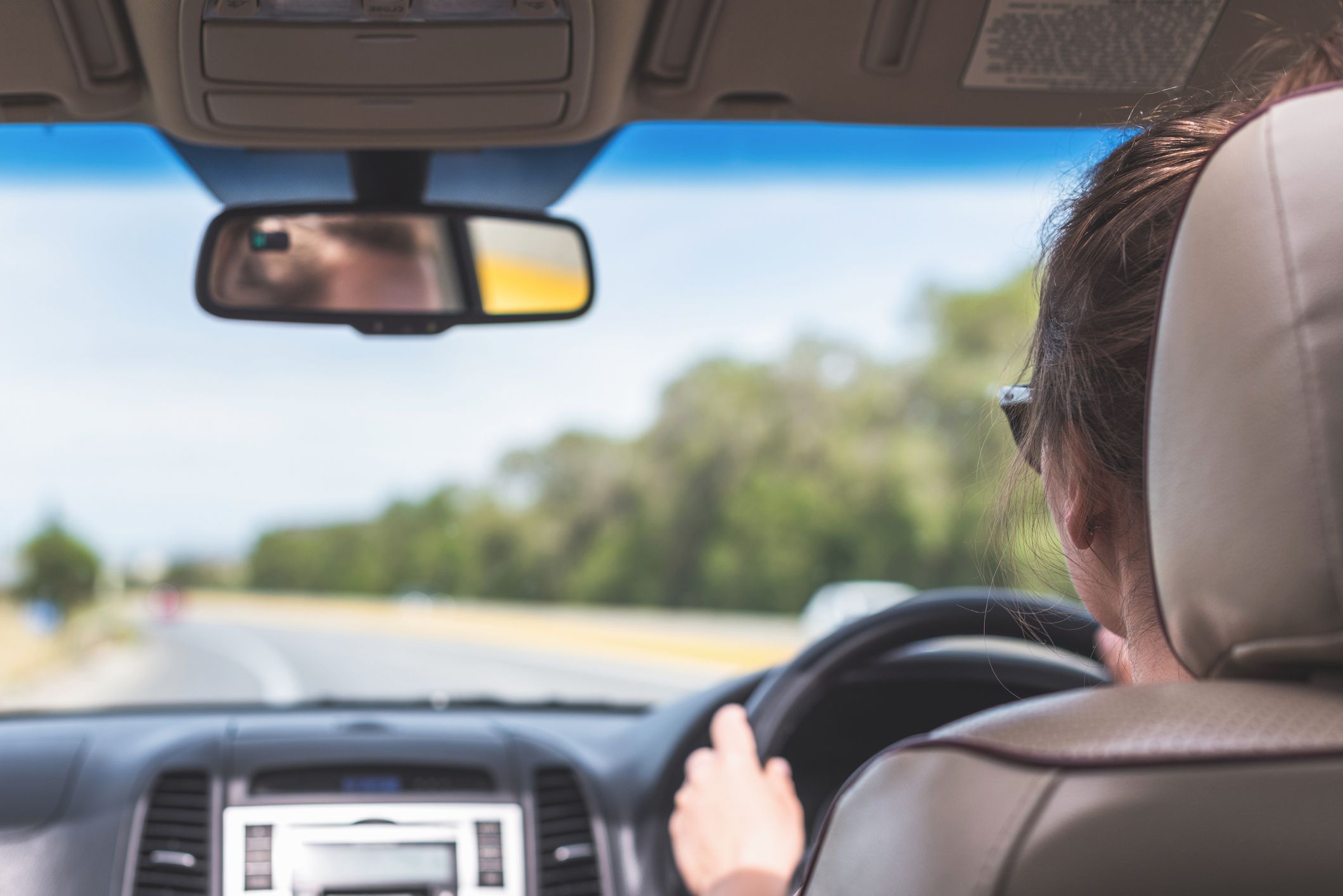A picture of a woman driving a car taken from behind. 
