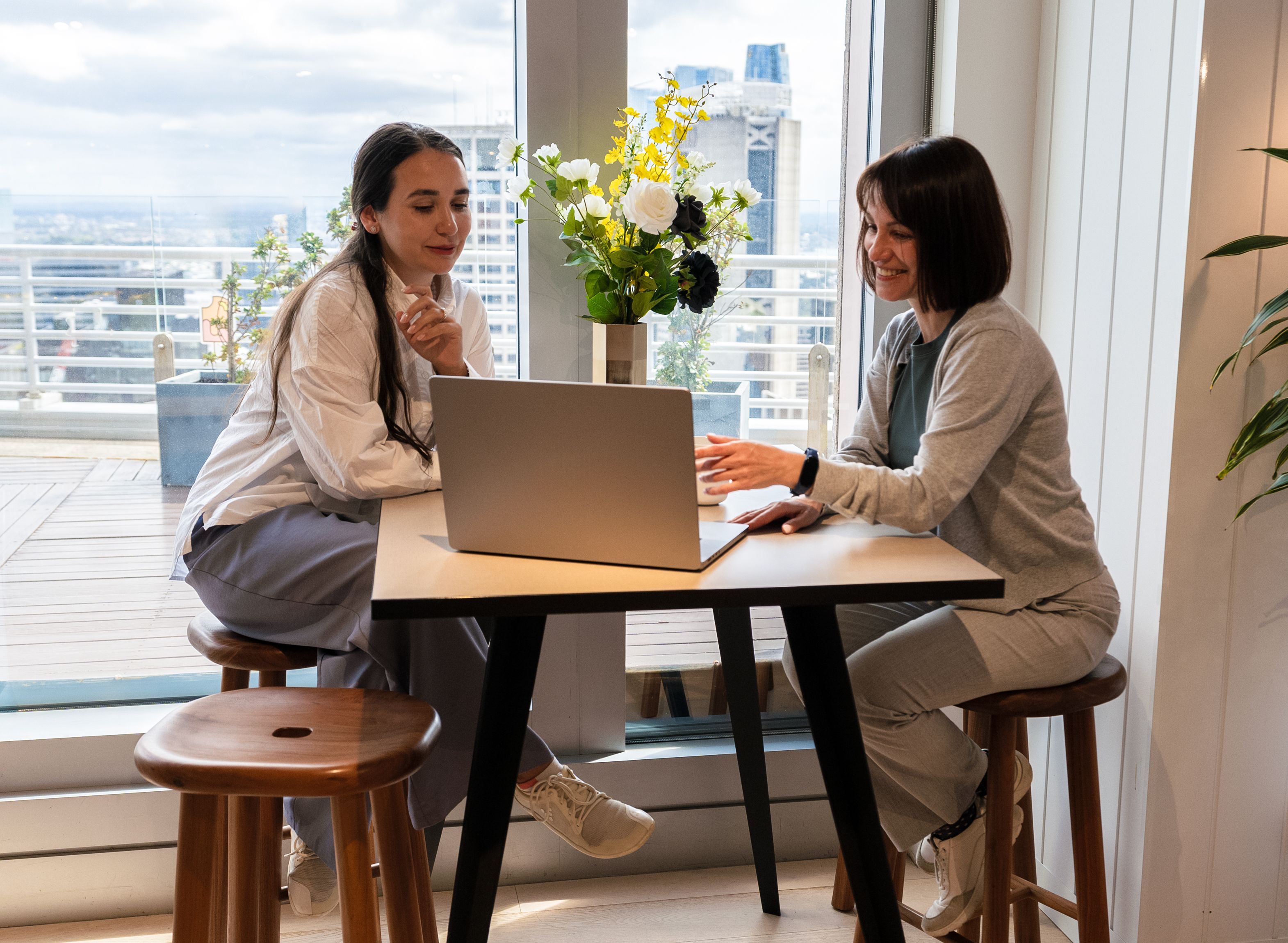 Bella and her colleague sit and talk while looking at a laptop together.