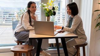 Bella and her colleague sit and talk while looking at a laptop together.