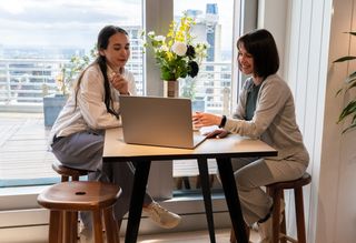 Bella and her colleague sit and talk while looking at a laptop together.