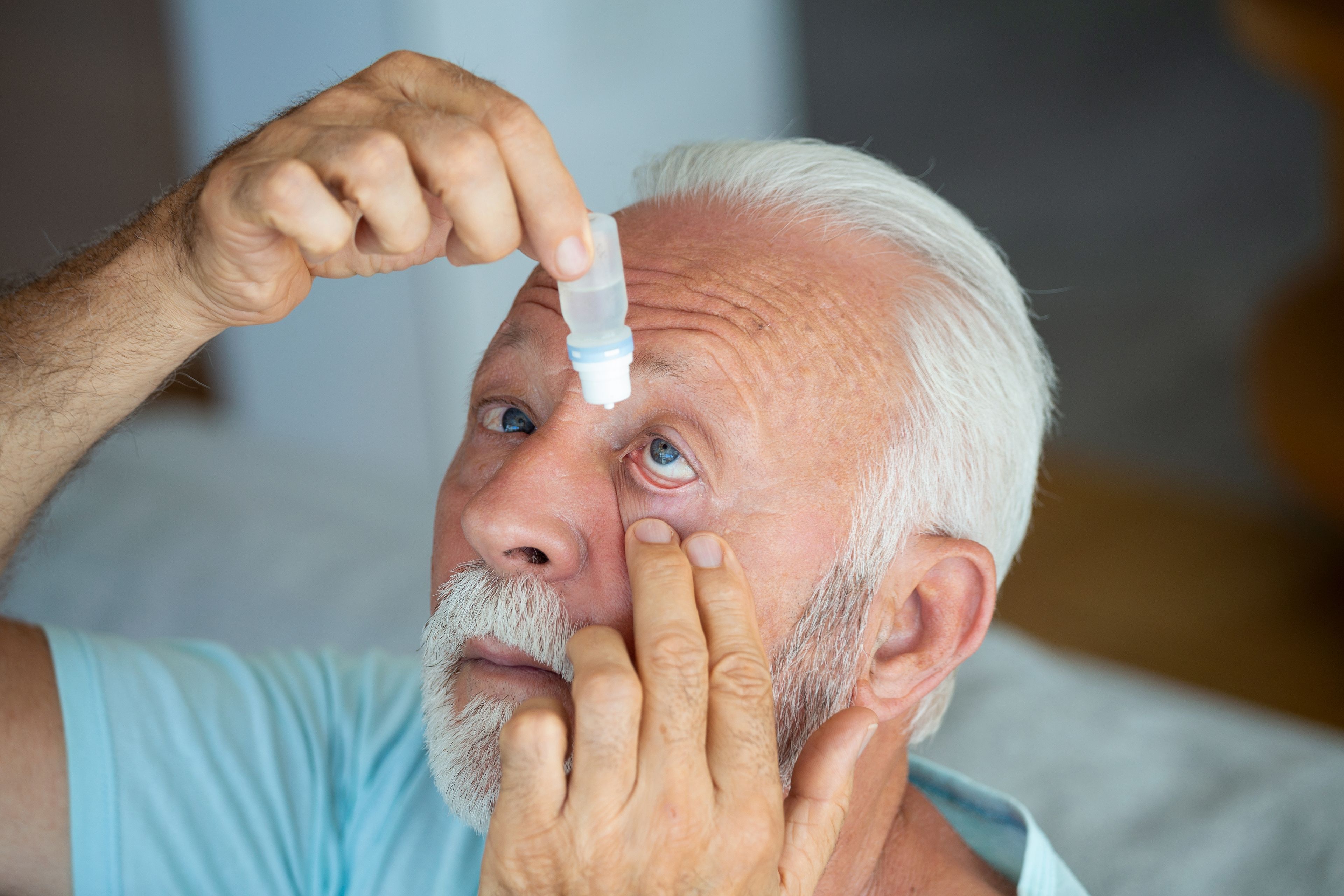 Older person using eye drops with their head titled slightly back