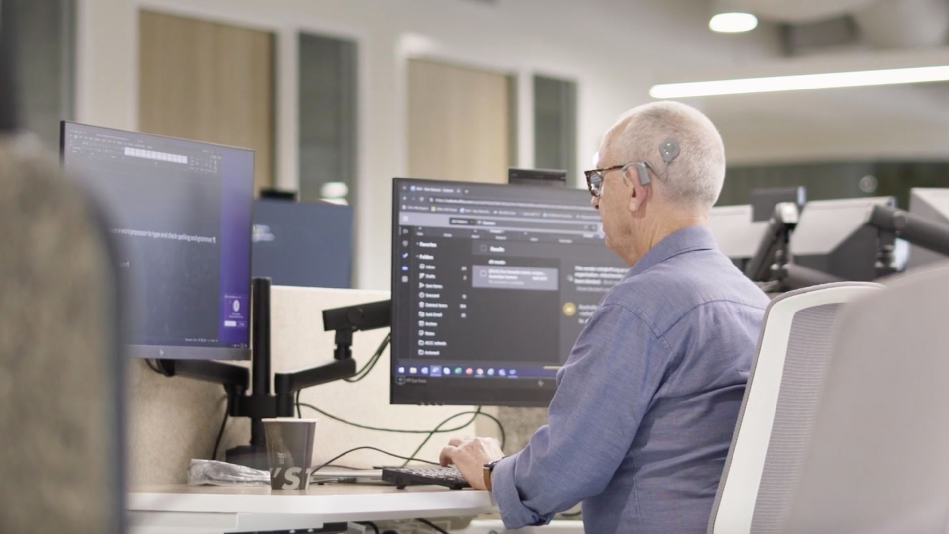 A man works at his desk using two monitors with magnified screens.