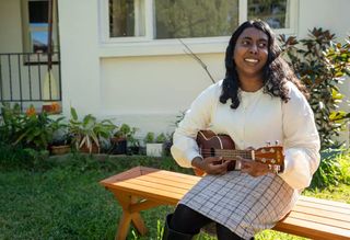 Abby playing her ukulele on a bench in her garden