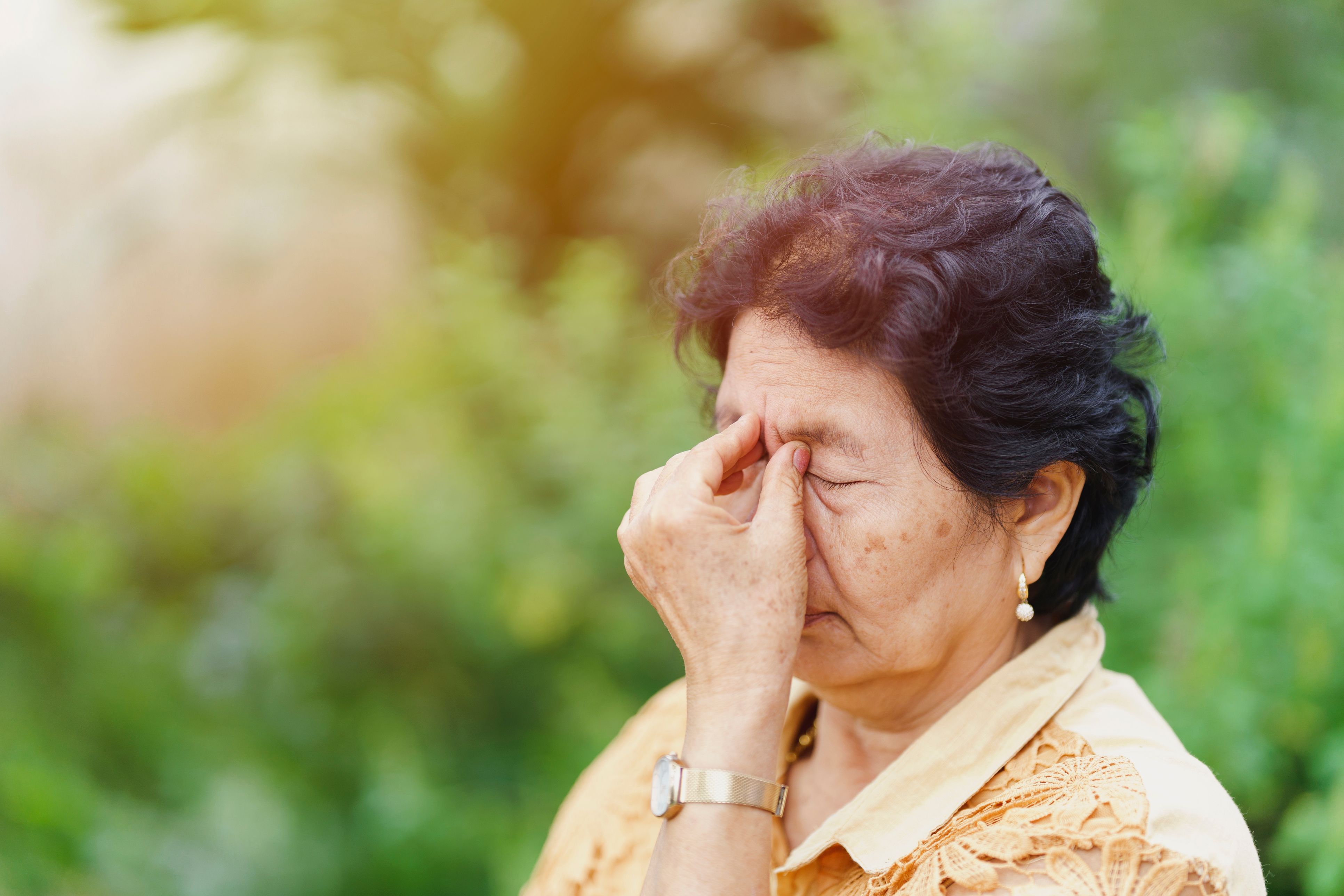 A woman rubbing her eyes outside. 