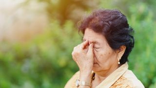 A woman rubbing her eyes outside.