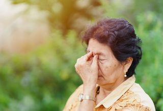 A woman rubbing her eyes outside.