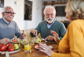 Group of older people smiling and laughing while eating at home