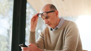 A man lifts his glasses to look at his phone screen