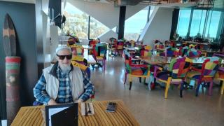 Laurence wears his Meta glasses sitting in a café filled with brightly coloured chairs.