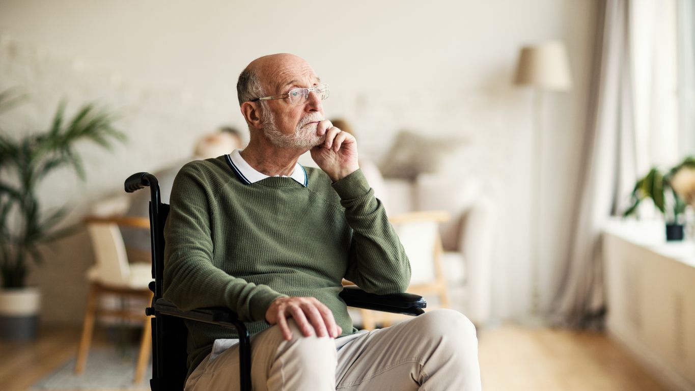 Older man in wheelchair looking pensive at home