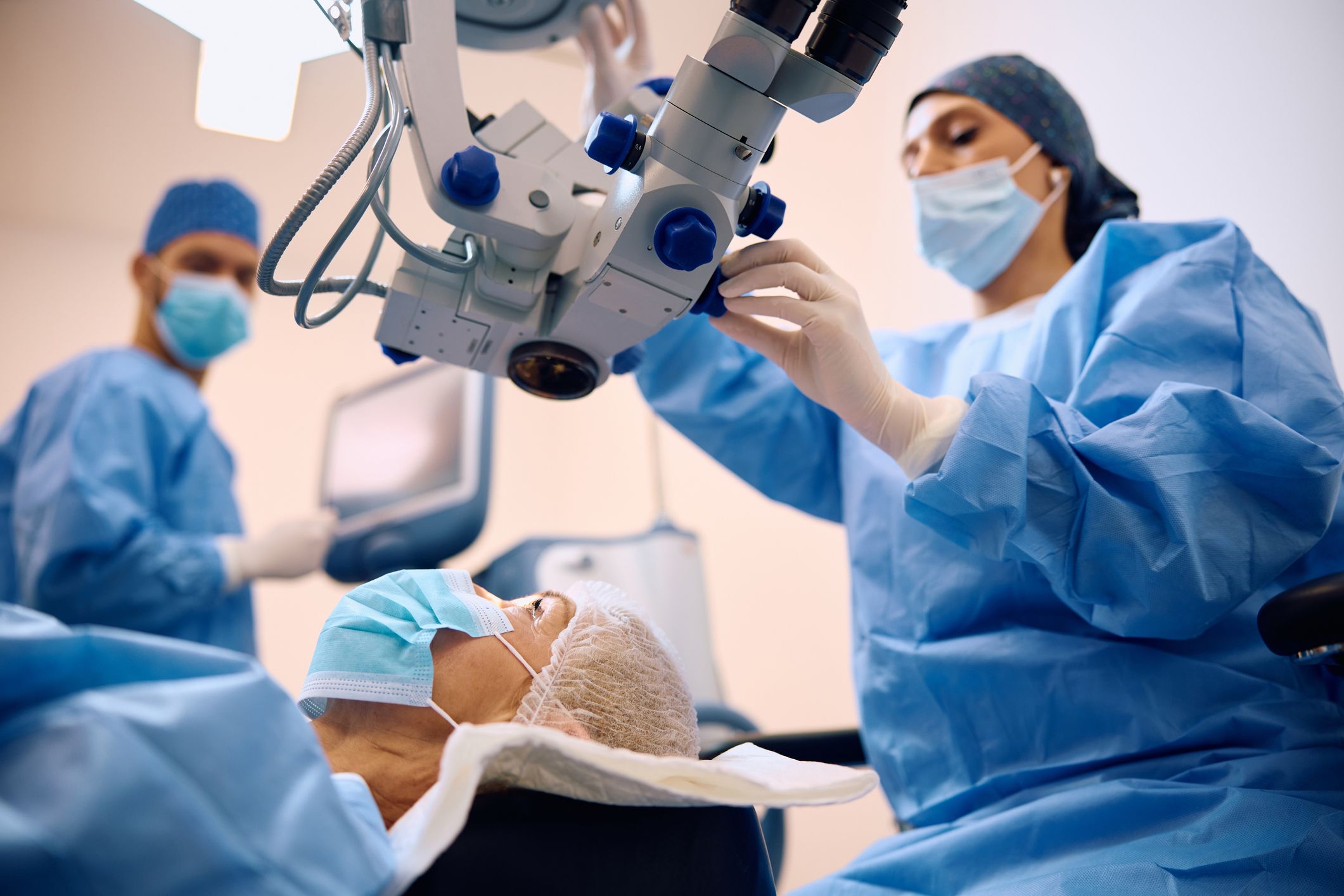An ophthalmologist preparing equipment for cataract surgery with a patient lying on the surgery bed.