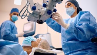 An ophthalmologist preparing equipment for cataract surgery with a patient lying on the surgery bed.