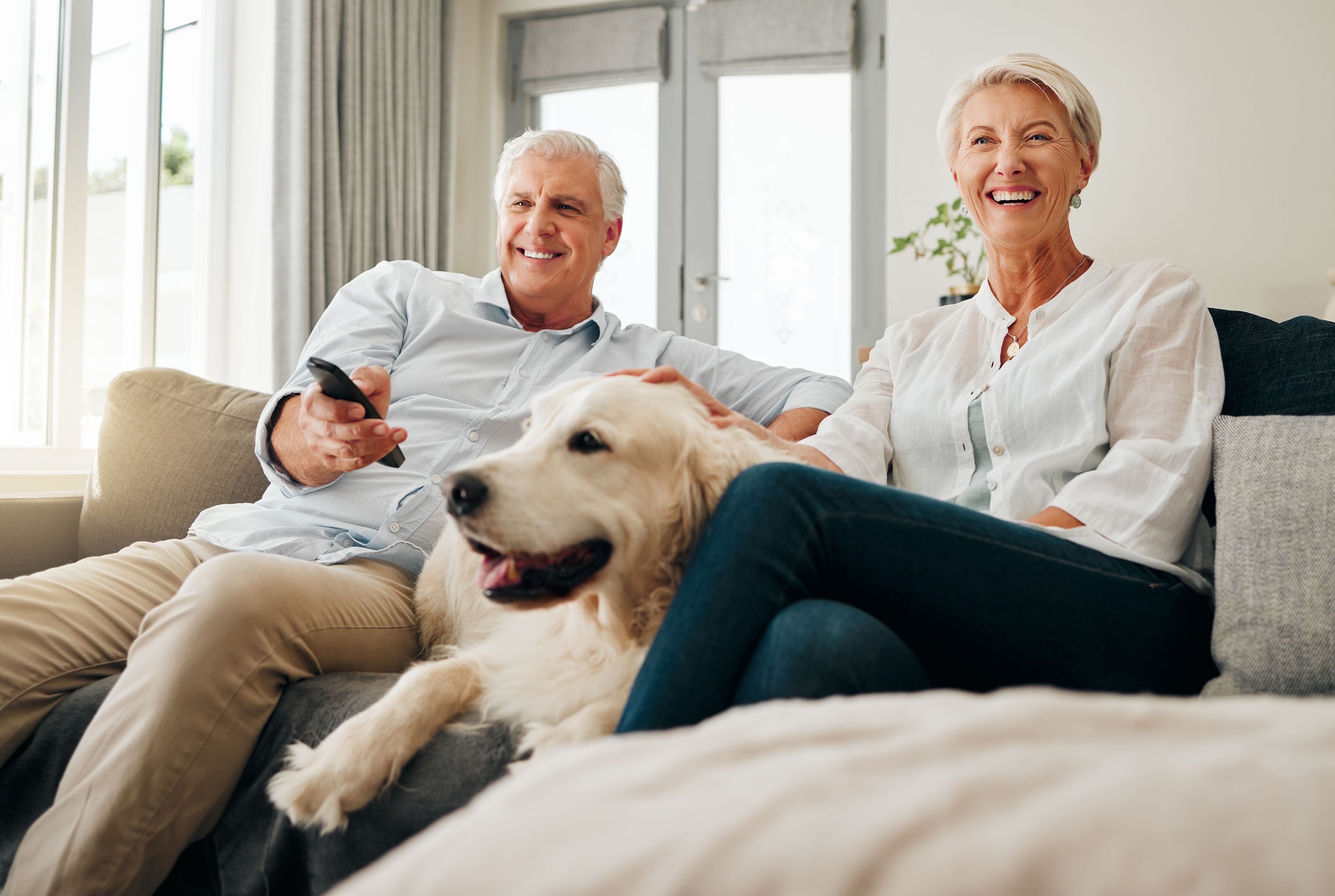 Older couple sitting on couch with dog watching television