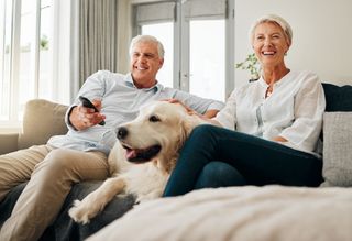 Older couple sitting on couch with dog watching television