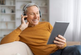 Smiling older person wearing headphones and using digital tablet