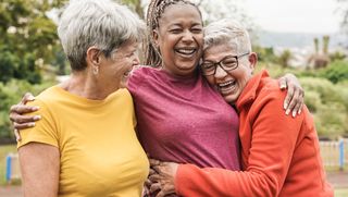 Group of three older people hugging outdoors