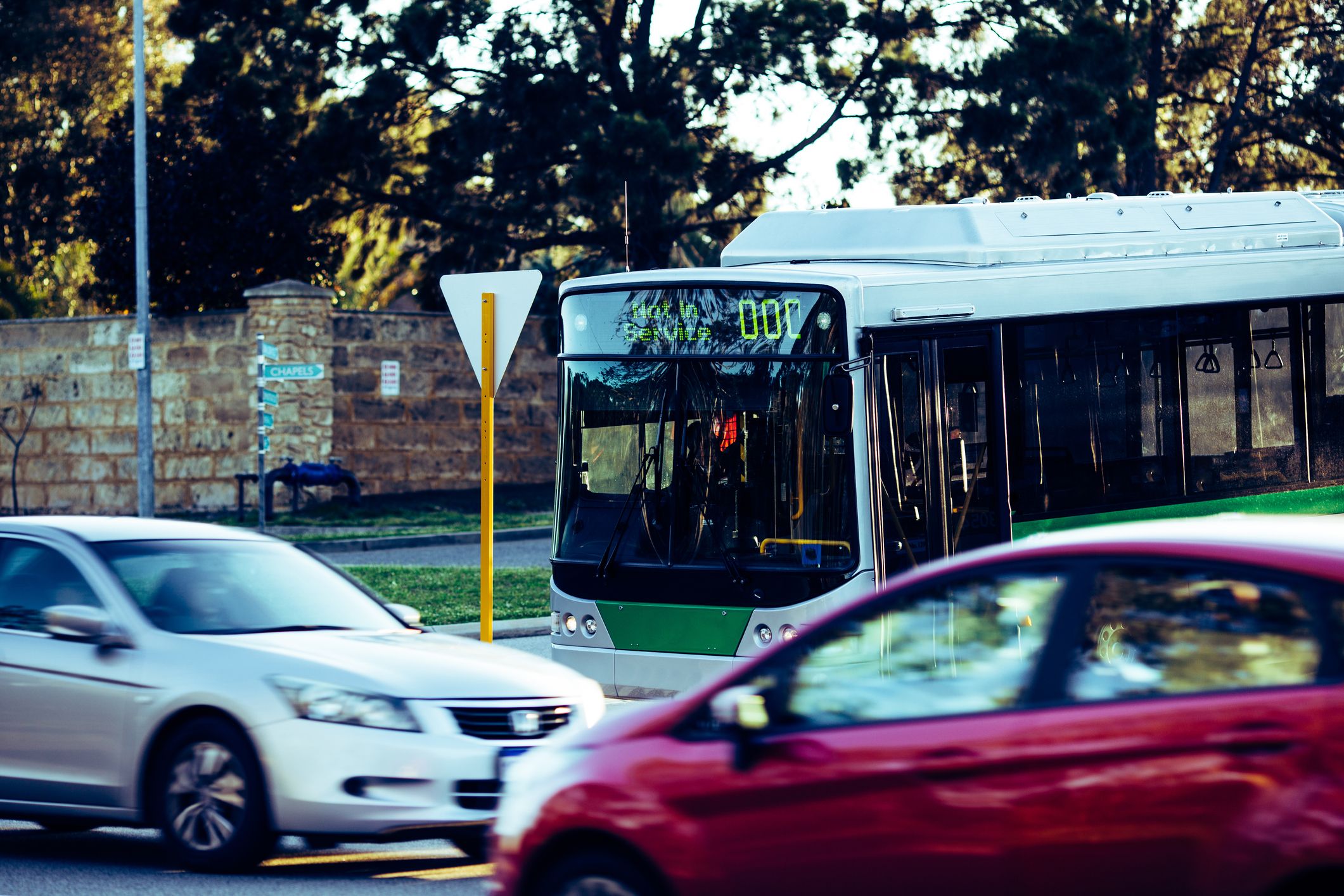 Two cars drive past a bus at an intersection.