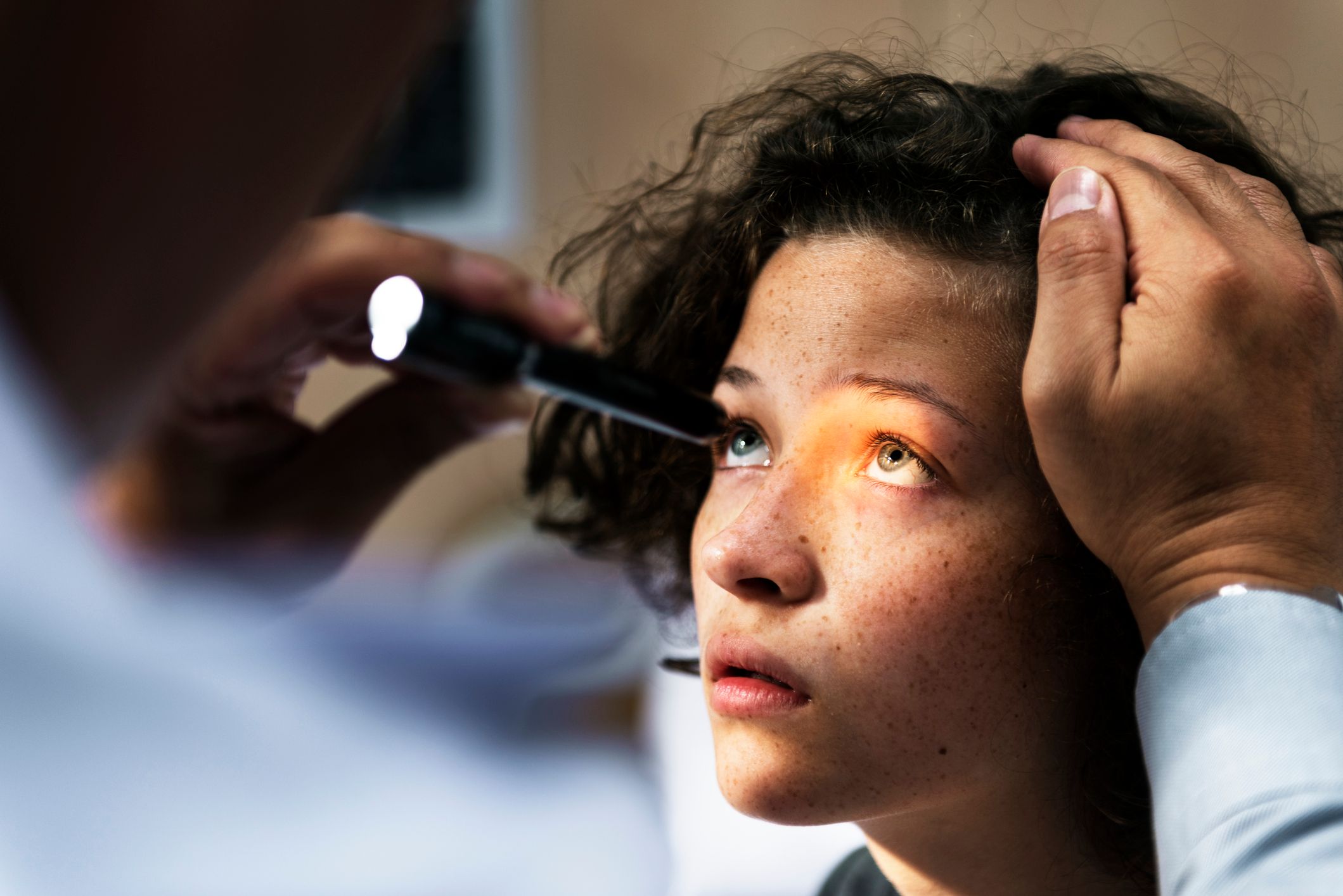 A child having their eyes examined with a penlight.