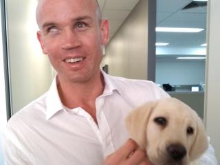 Ben Moxey smiling at the camera holding a yellow Labrador puppy.