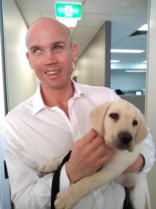 Ben Moxey smiling at the camera holding a yellow Labrador puppy.