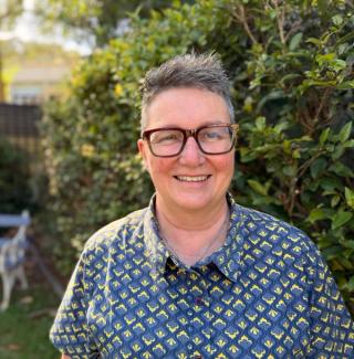 A photo of Nerida smiling at the camera standing in front of a hedge.