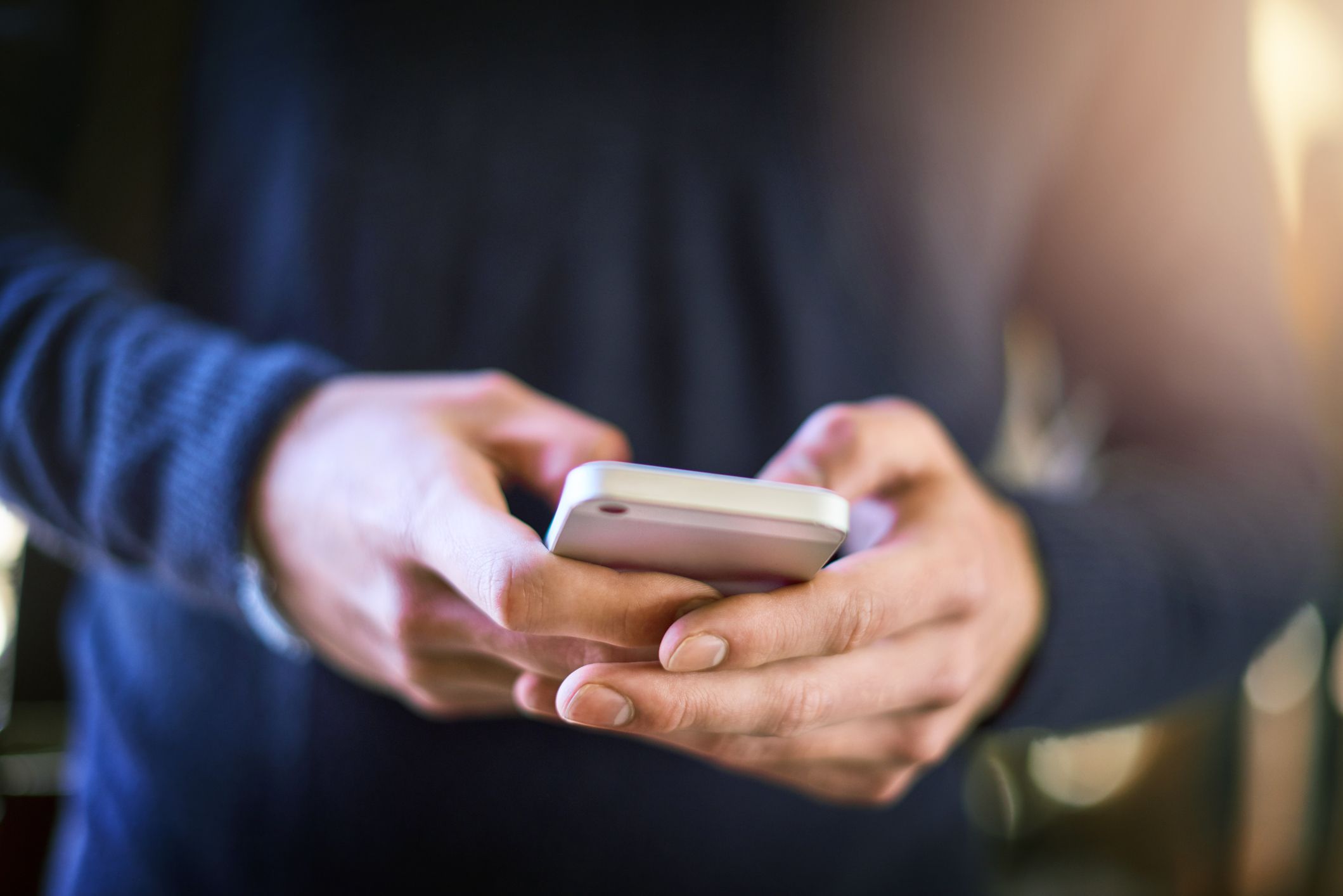 A close up of a man typing on a smartphone with two hands. 
